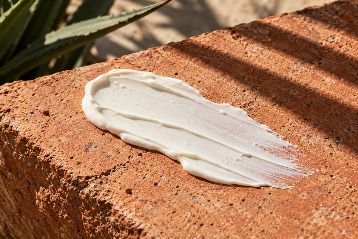 Lightweight mineral sunscreen lotion swatched over terracotta stone in bright daylight.